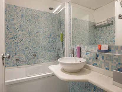 Bagno a mosaico con vasca e lavabo della camera Doppia Executive