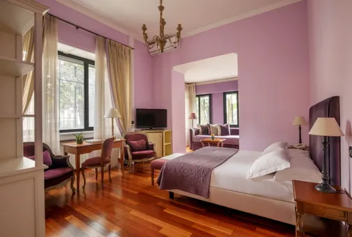 Junior Suite del Fenix Hotel Roma nei toni del viola, con letto matrimoniale e zona salotto