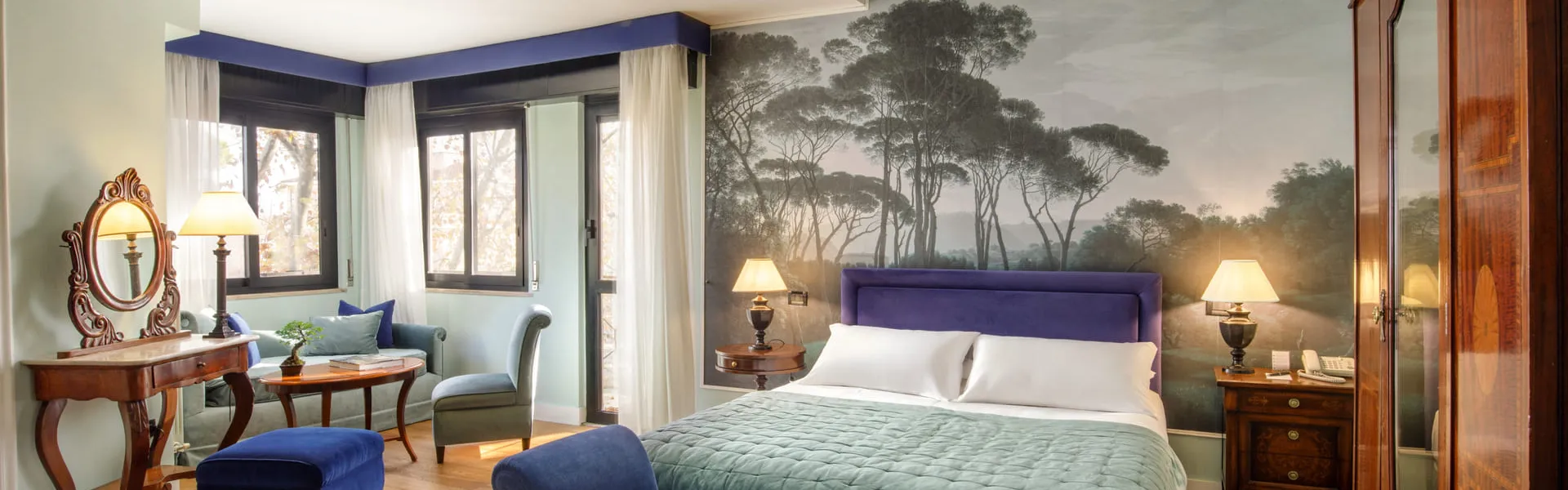 Camera del Fenix Hotel Roma con carta da parati a pini, letto matrimoniale e dormeuse in velluto blu