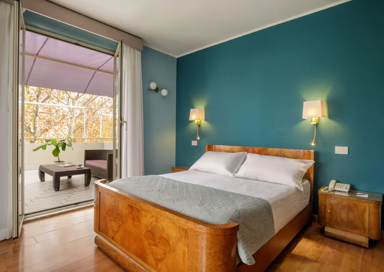 Camera con parete color petrolio, letto in radica e porta-finestra sul terrazzino